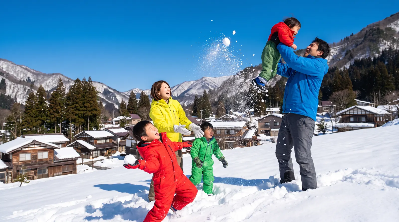 晴れた雪の山あいの村で、雪合戦をして笑う家族